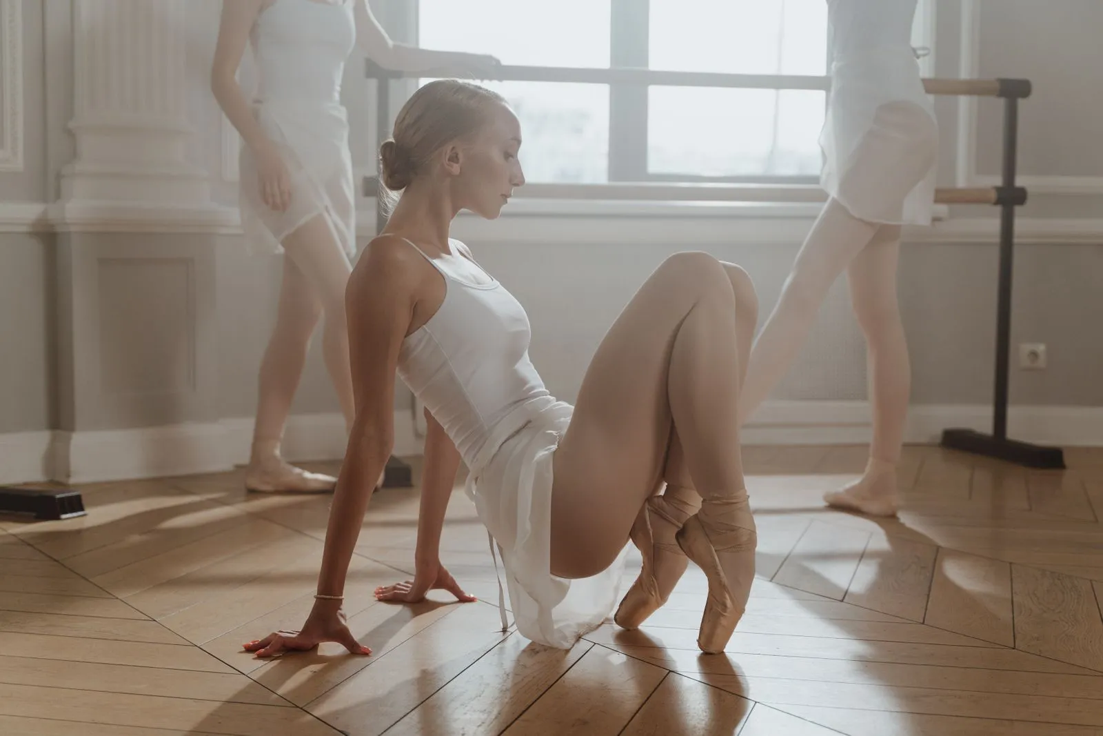 Ballet dancers practicing graceful moves in a sunlit studio setting.
